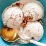 A gold spoon sits in a turquoise bowl with 3 scoops of vegan ice cream.