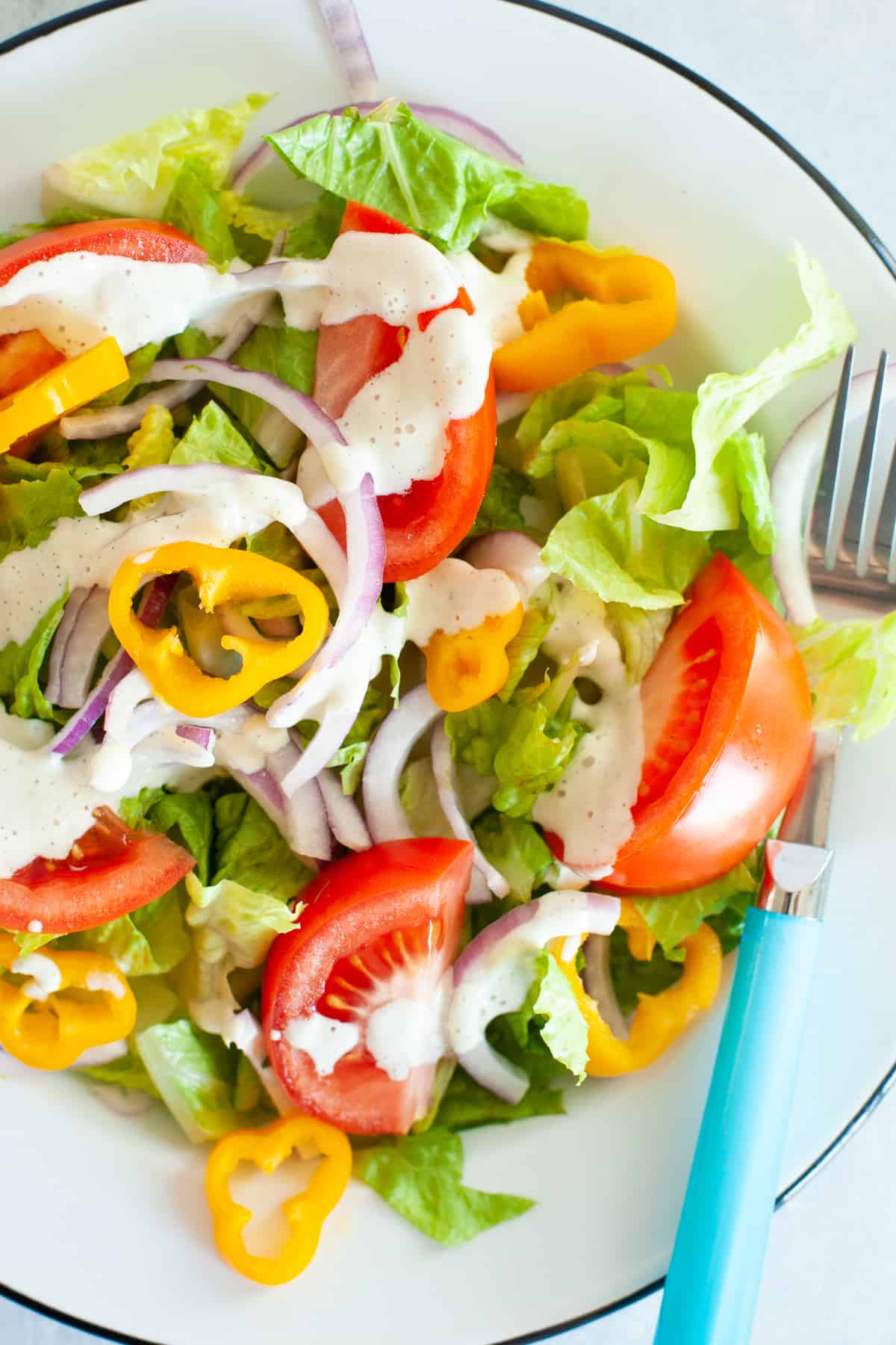 A white bowl is filled with a colorful salad dressed with dairy-free cashew ranch dressing.
