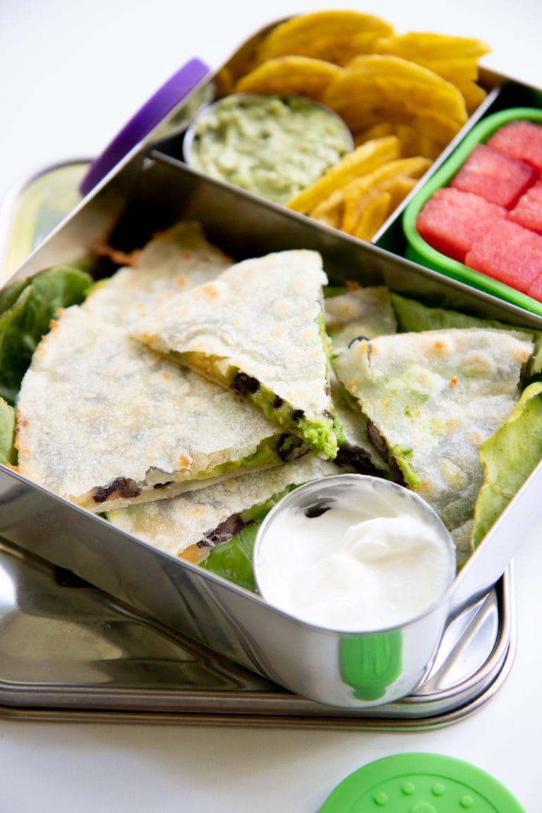 A quesadilla packed into a lunch box with a condiment cup of sour cream