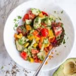 Avocado Bell Pepper Salad sits in a white bowl on a white background. A Lemon sits nearby.
