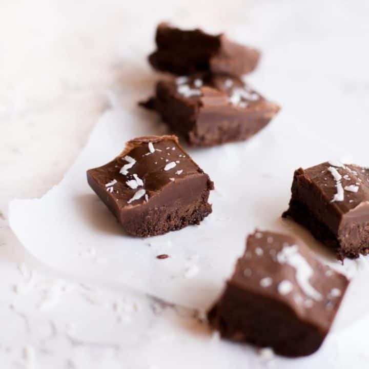 Squares of vegan fudge sprinkled with coconut on parchment paper.