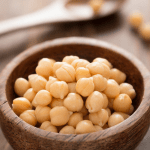 A wooden bowl of cooked chickpeas on a wooden table.