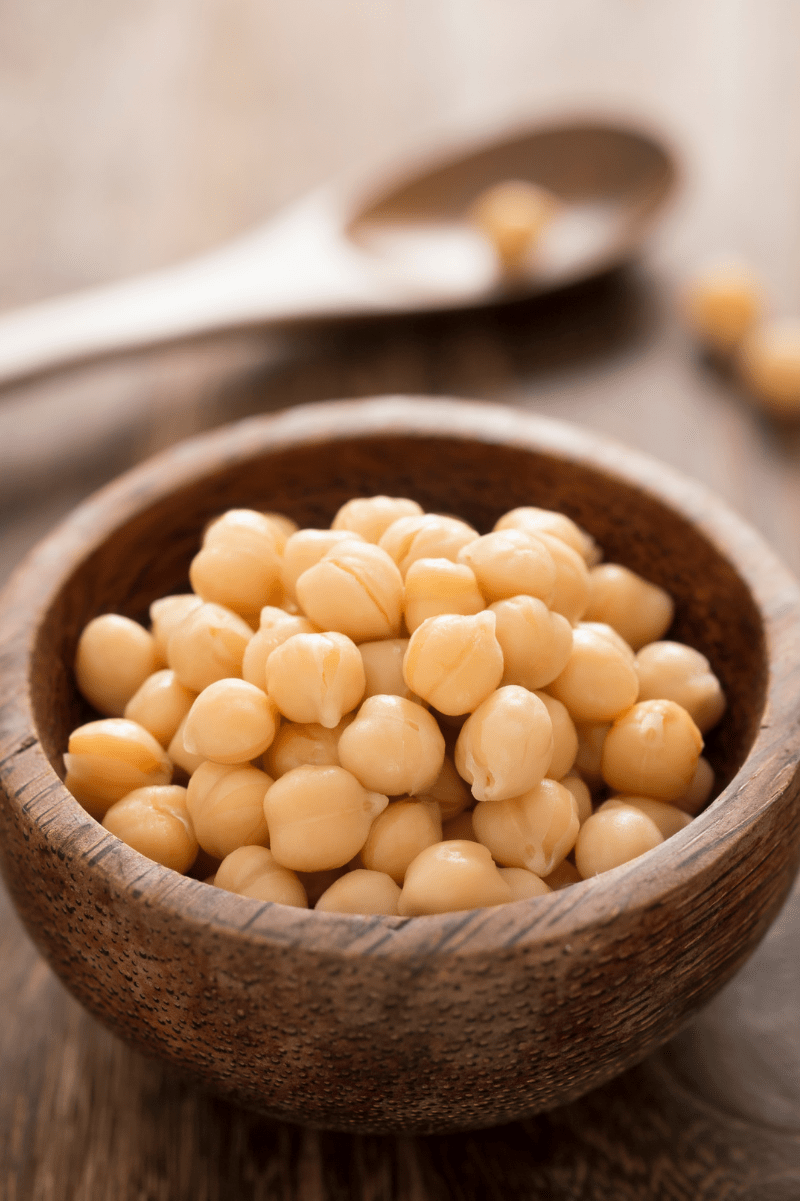 A wooden bowl of cooked chickpeas on a wooden table.
