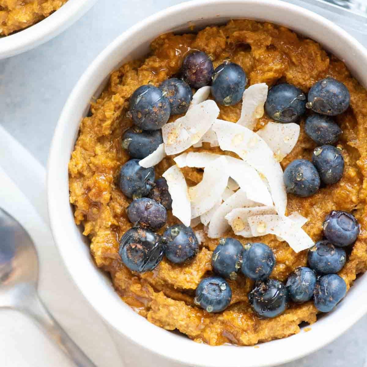 Two bowls of pumpkin coconut porridge with blueberries on top sit on a gray countertop