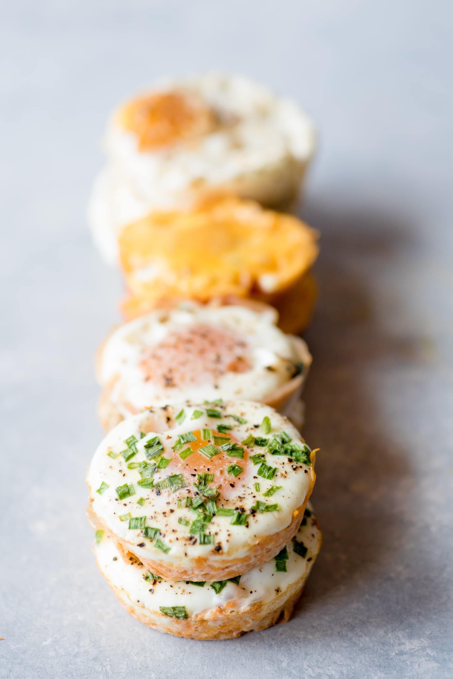 Four stacks of egg muffin cups rest on a grey background. The front stack is topped with chopped herbs.