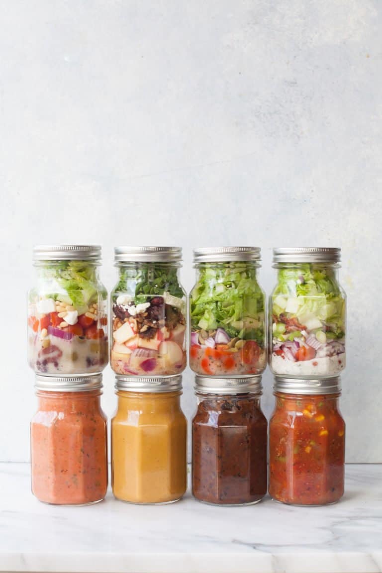 Eight glass mason jars stacked, half with salads, and half with soups on a gray background