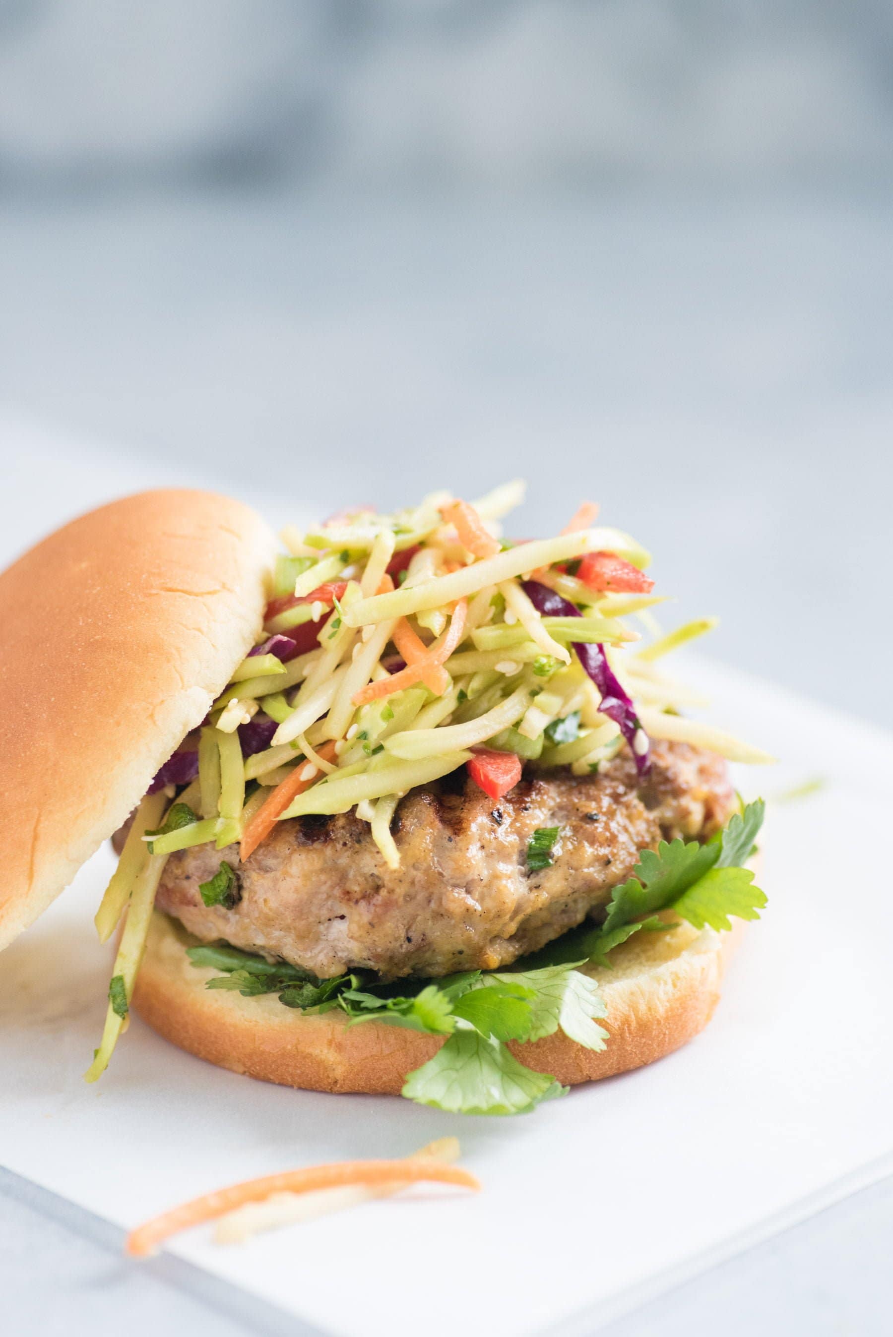 Close up side shot of Asian pork burger with broccoli slaw on top, served on a bun