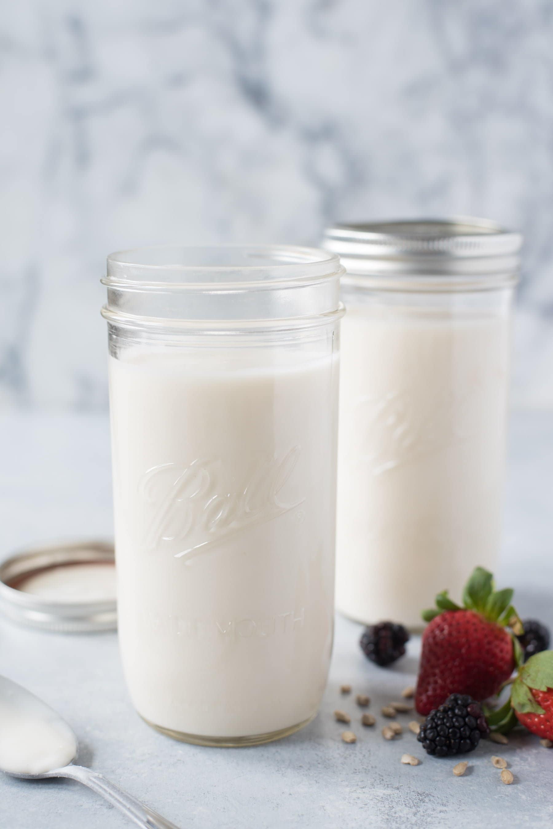 Side shot of two tall Ball mason jars filled with coconut yogurt, with berries off to the side