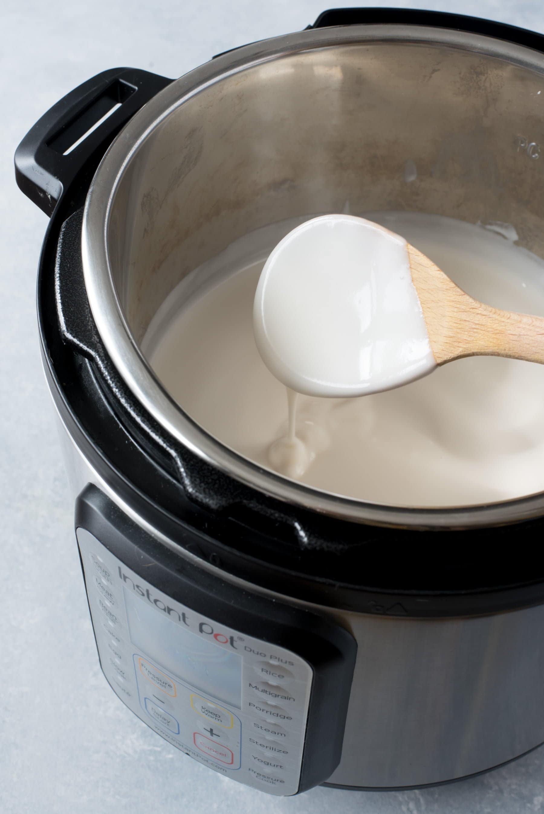 Side angle shot of wooden spoon scooping coconut yogurt from an Instant Pot