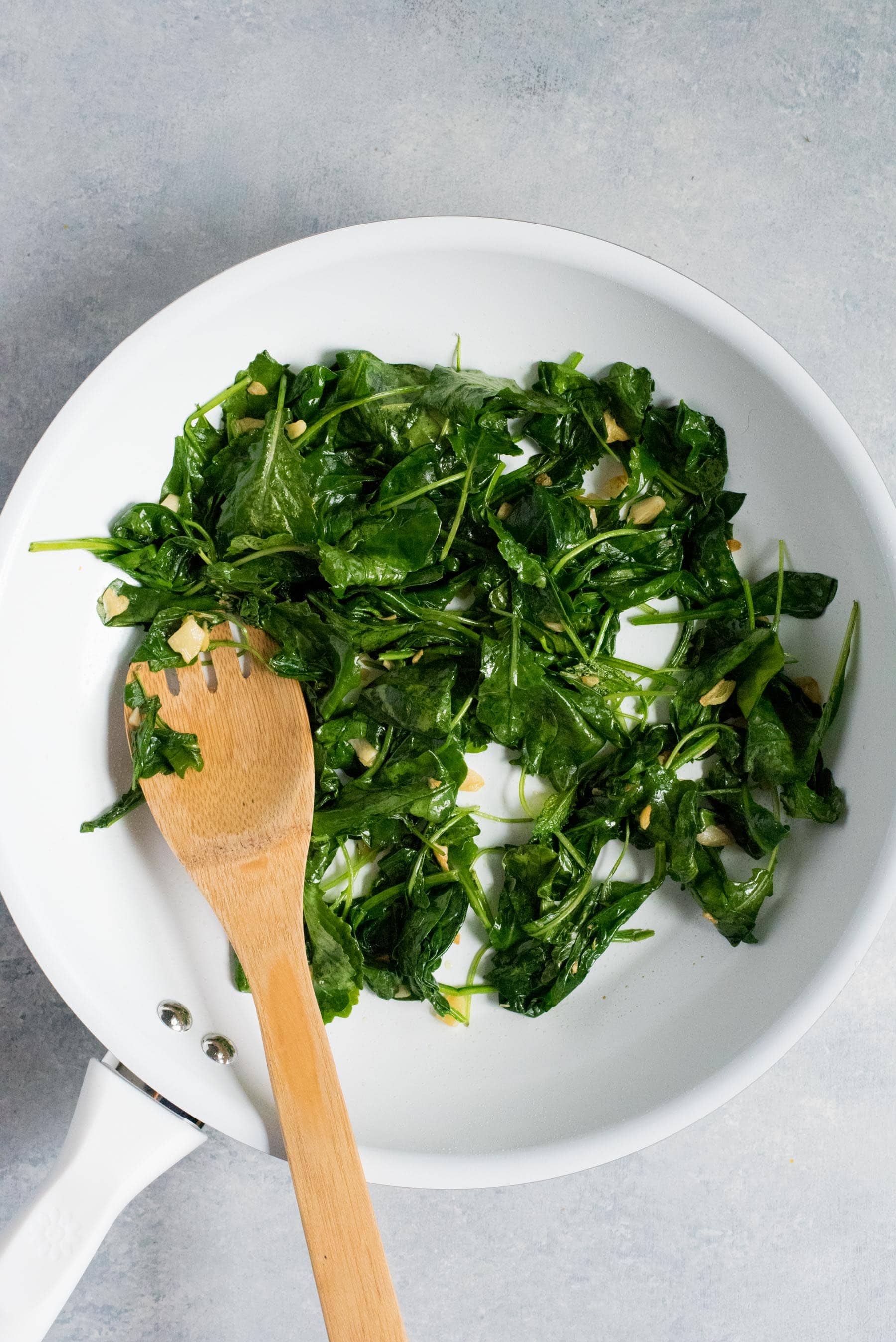 Overhead shot of wilted greens in a white bowl with a wooden spoon