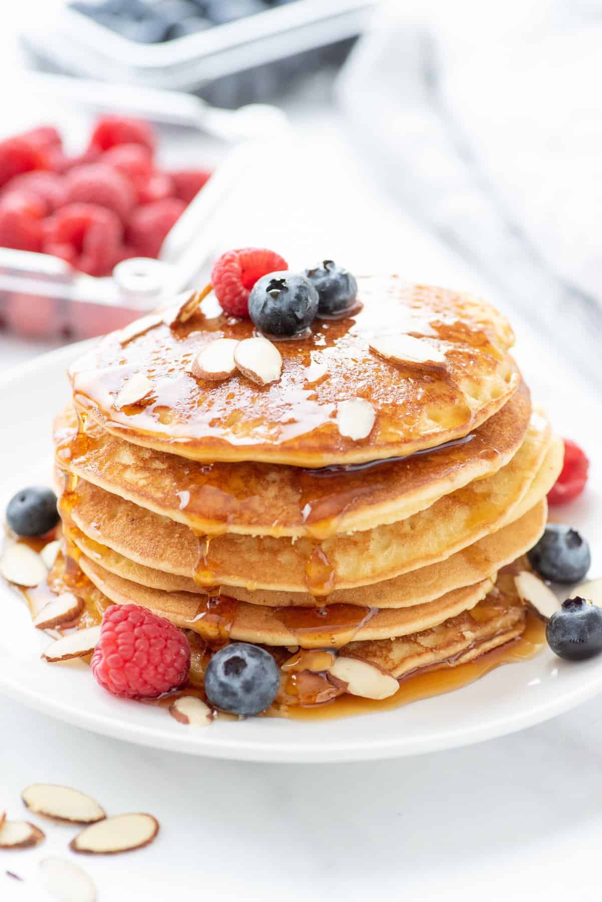 Side angle shot of a stack of grain-free blender almond pancakes, garnished with berries and sliced almonds