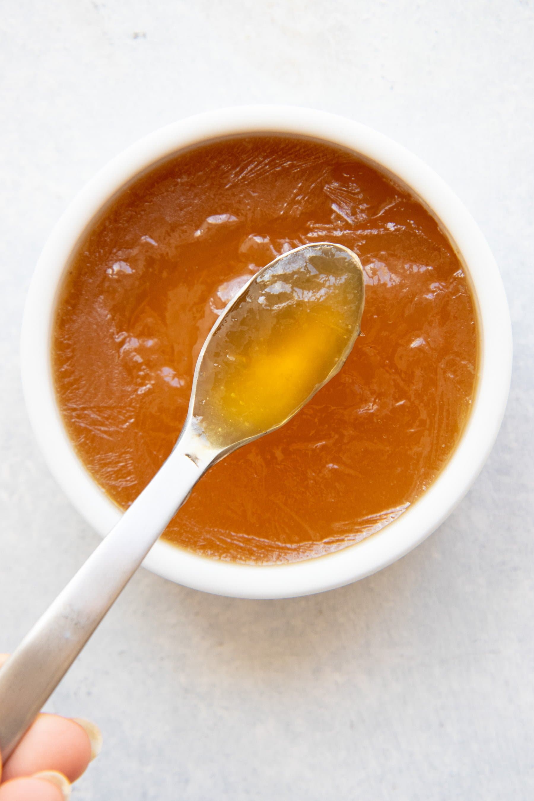 Overhead shot of a spoon in a white bowl of bone broth, demonstrating gel