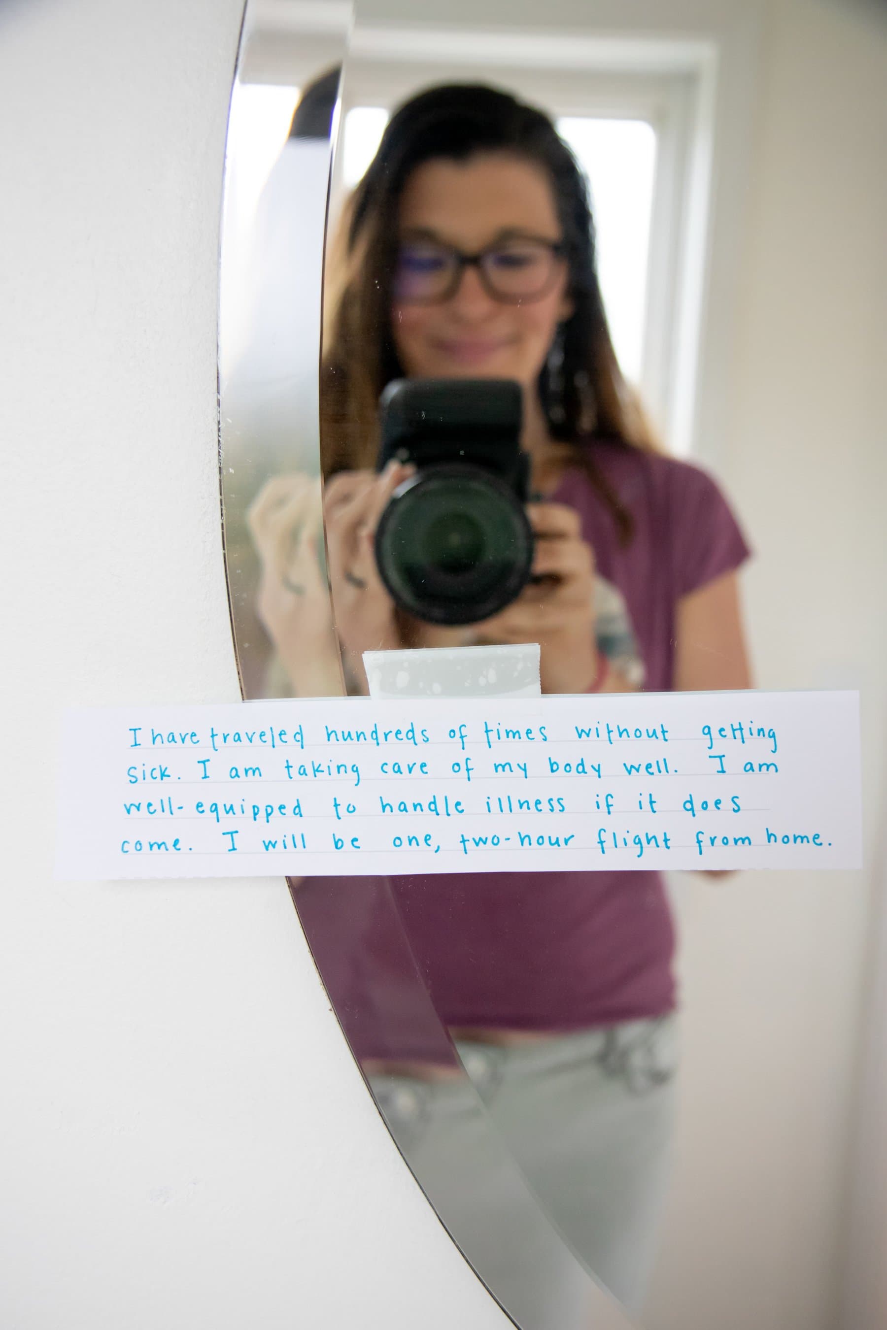 A woman takes a picture of her hand written note that is stuck to the mirror with a piece of tape.
