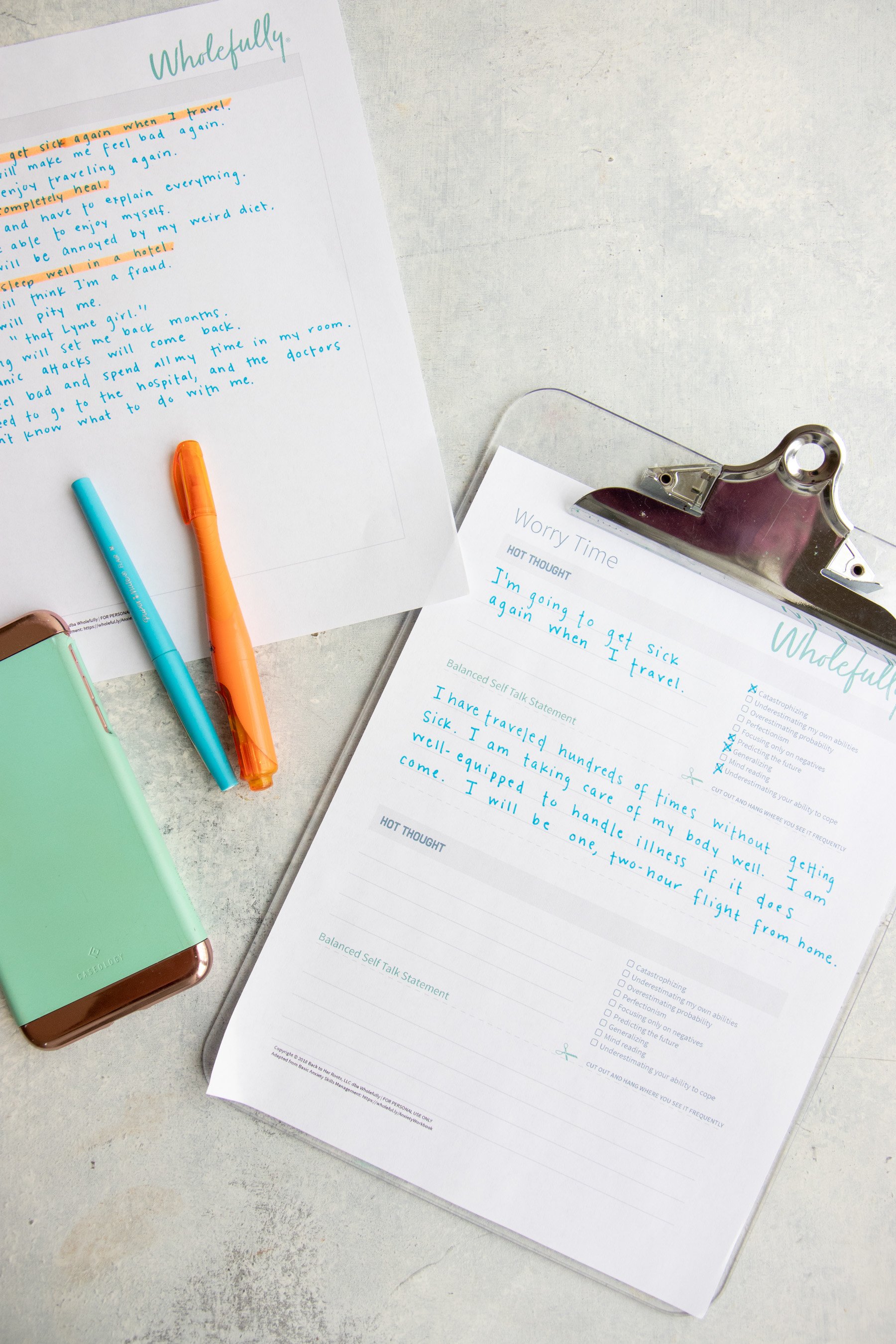 A clipboard holds a Worry Time worksheet with words written on it. A blue and orange highlighter sits on the left hand side, on top of a phone.