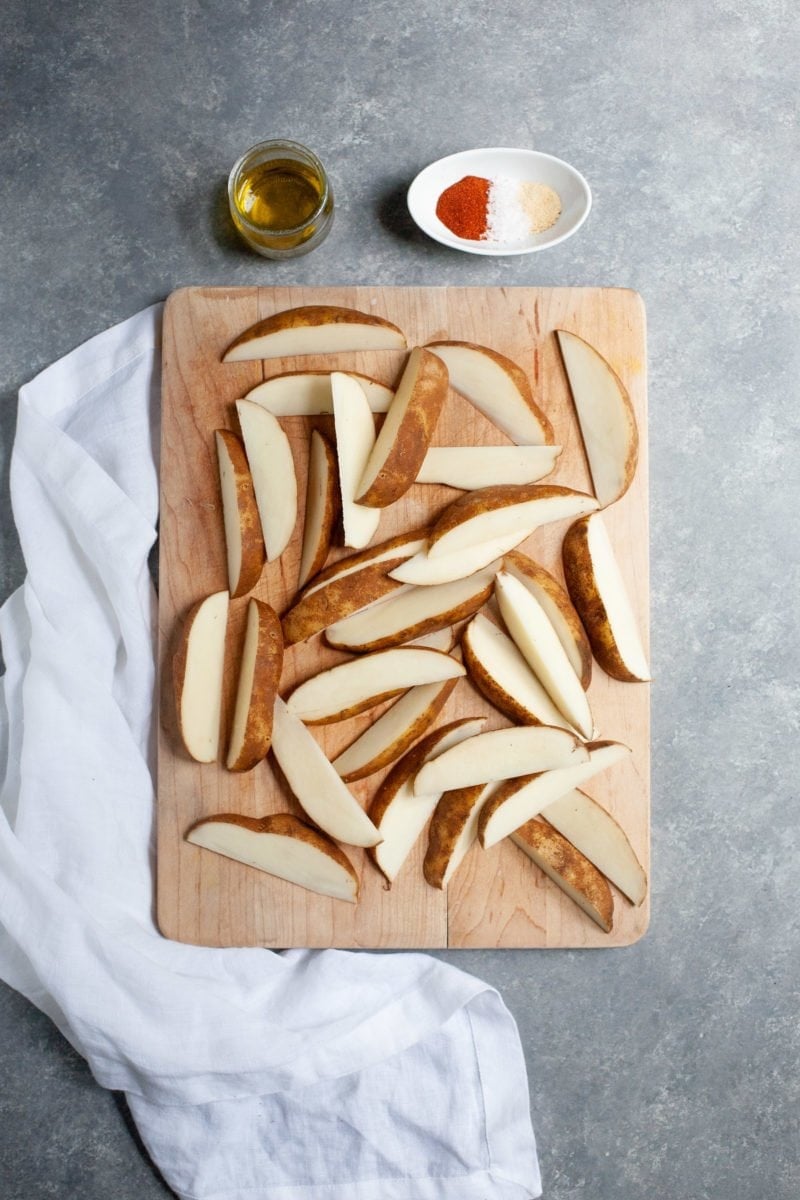 Overhead shot of potatoes cut into wedges on a wooden cutting board