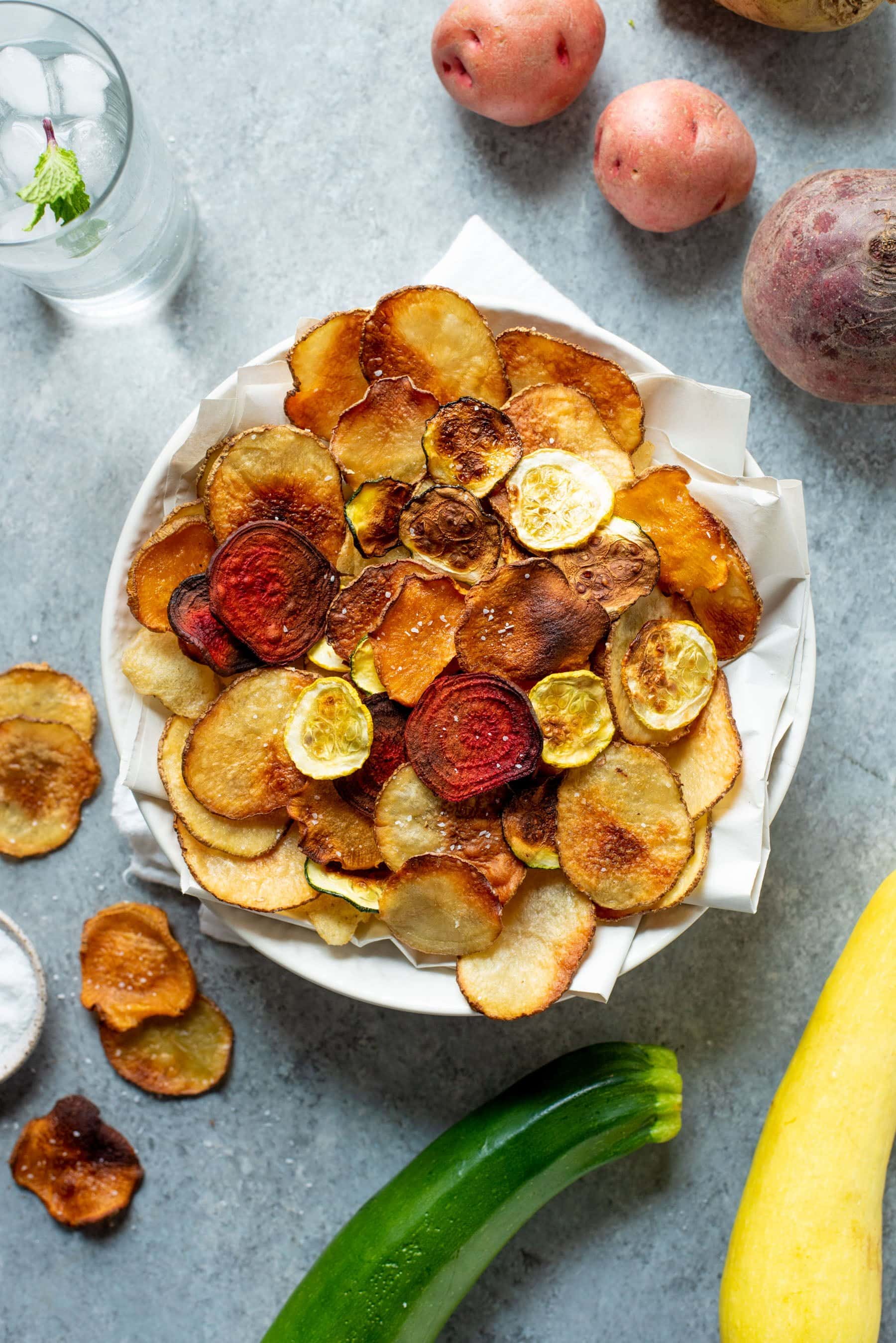 Overhead shot of Baked Vegetable Chips in a white bowl, surrounded by whole veggies