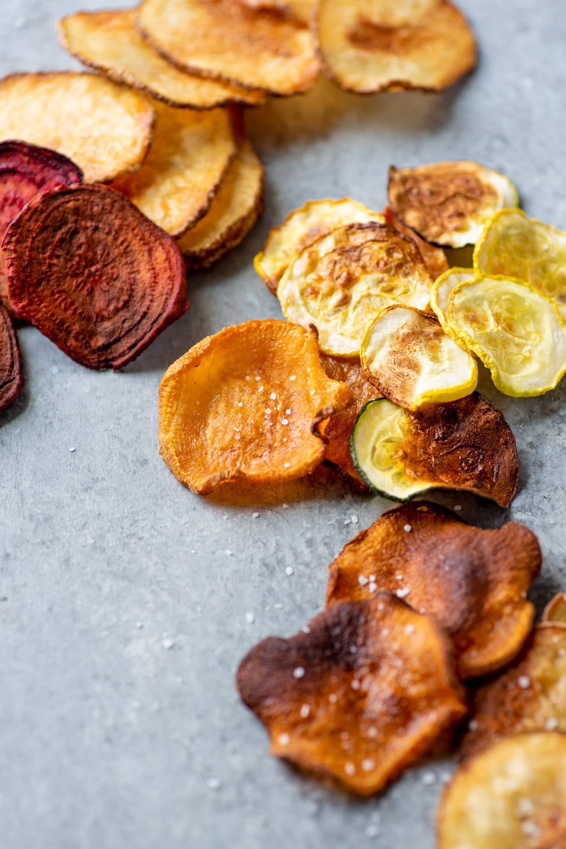 Baked vegetable chips spread out on a grey background