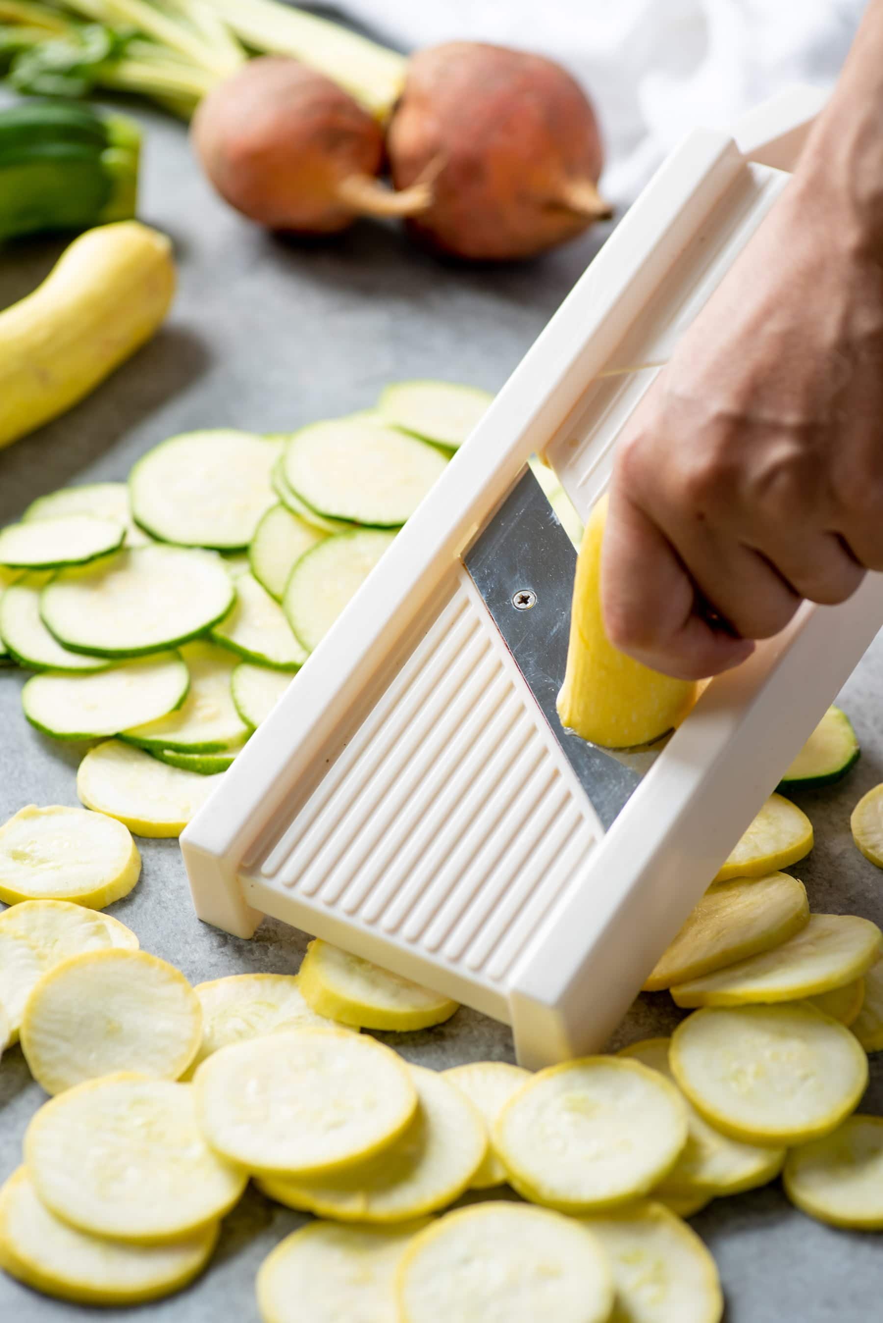 Hand slicing yellow squash and zucchini on a mandoline slicer