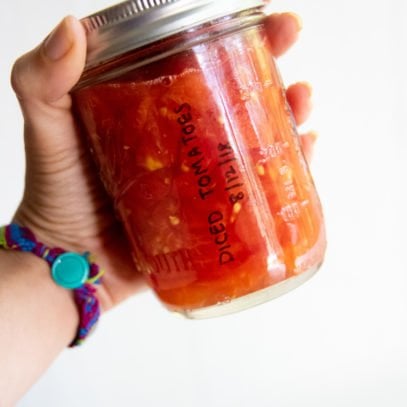 Hand holding a glass jar of canned diced tomatoes.