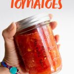 Hand holding a glass jar of canned diced tomatoes. A text overlay reads, "How to Can Diced Tomatoes, A Step-by-Step Tutorial for Beginners."