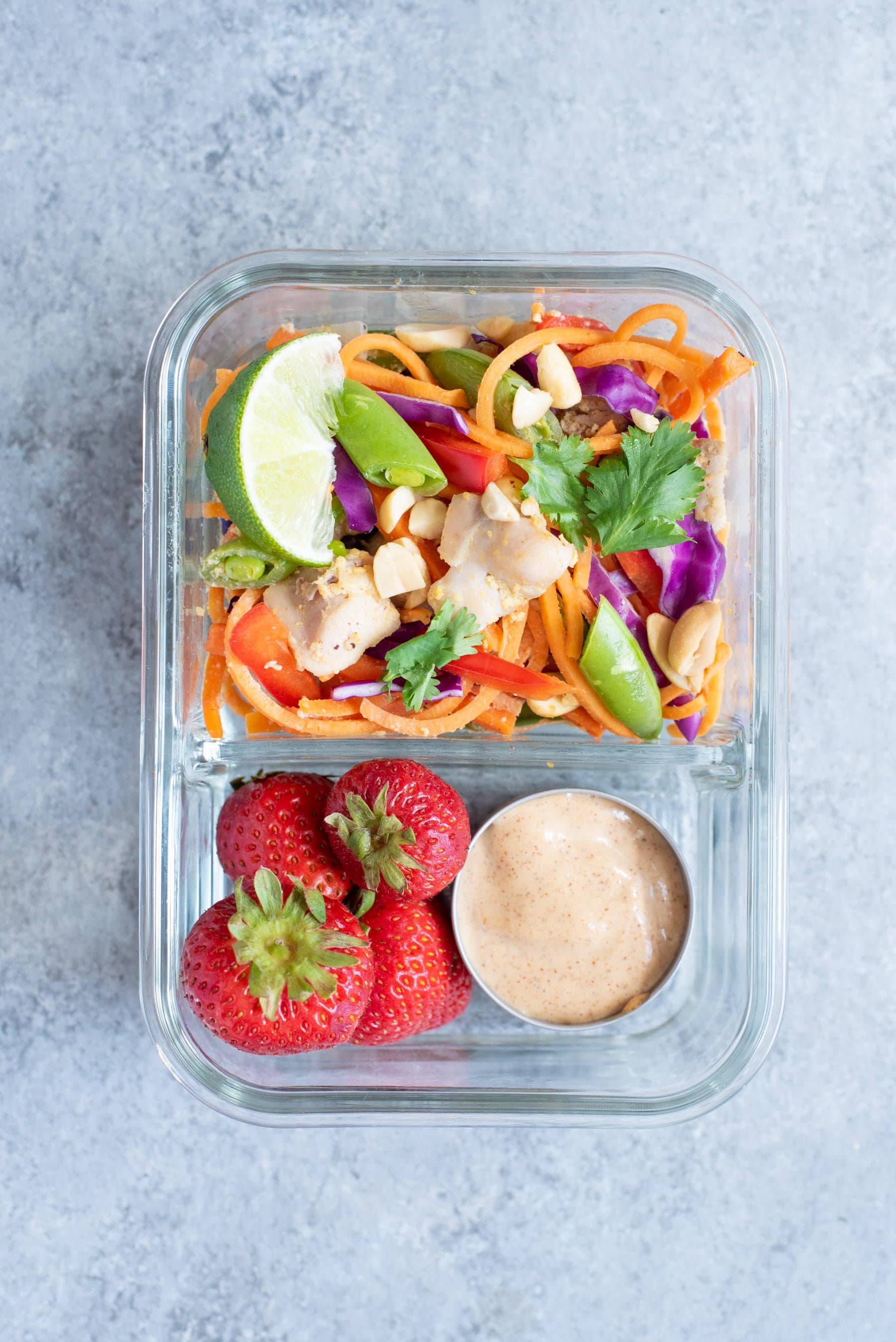 Overhead shot of Meal Prep Chicken Pad Thai with Sweet Potato Noodles packed into a glass lunch container with strawberries