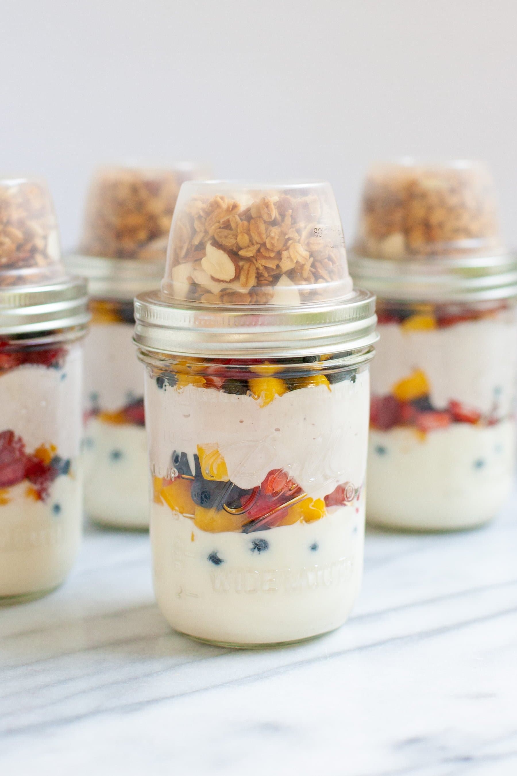 Meal Prep Fruit and Yogurt Parfaits in glass jars, with the granola in a separate cup on top