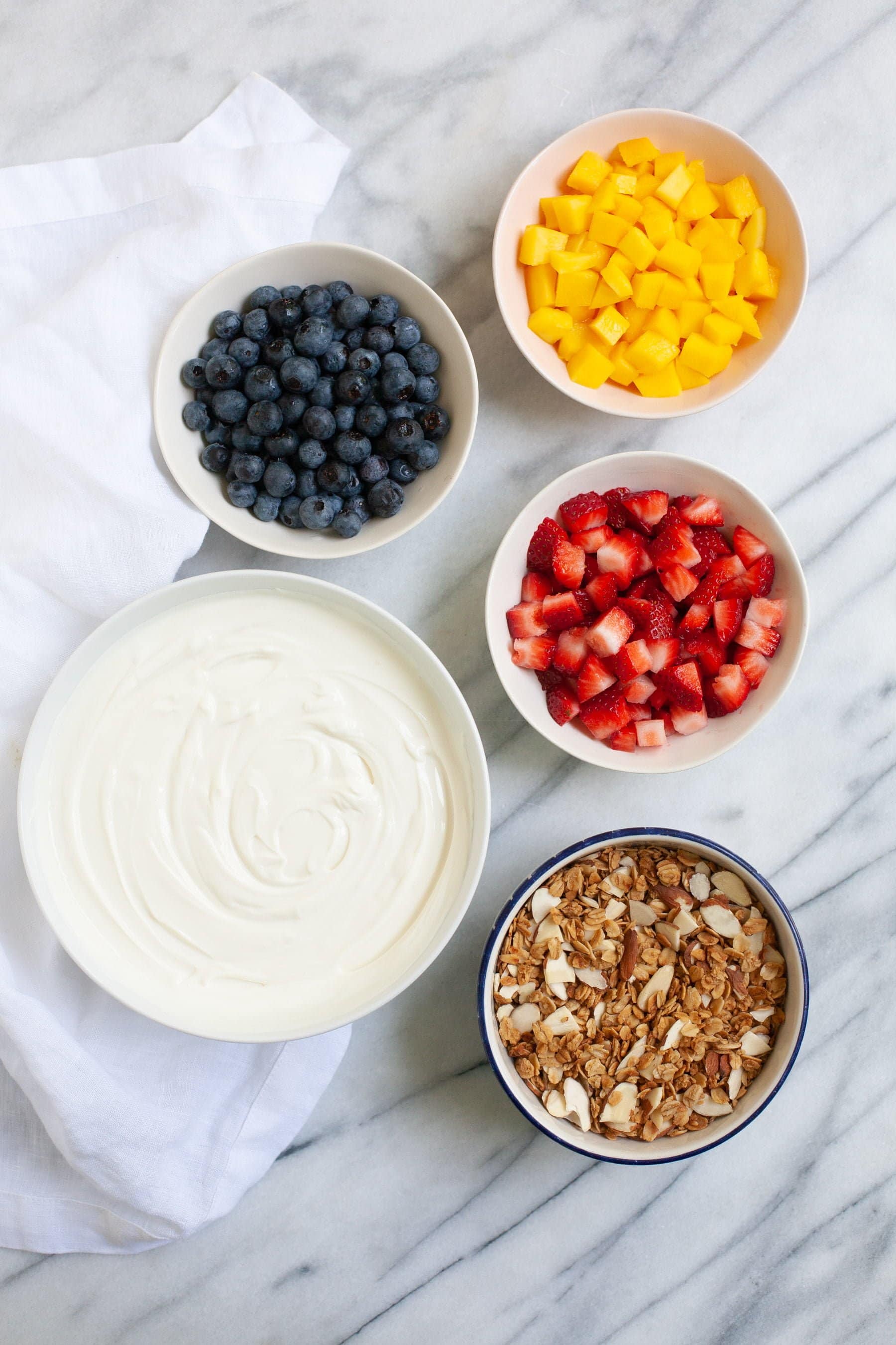 Overhead shot of ingredients for Meal Prep Fruit and Yogurt Parfaits - yogurt, fruit, and granola in bowls