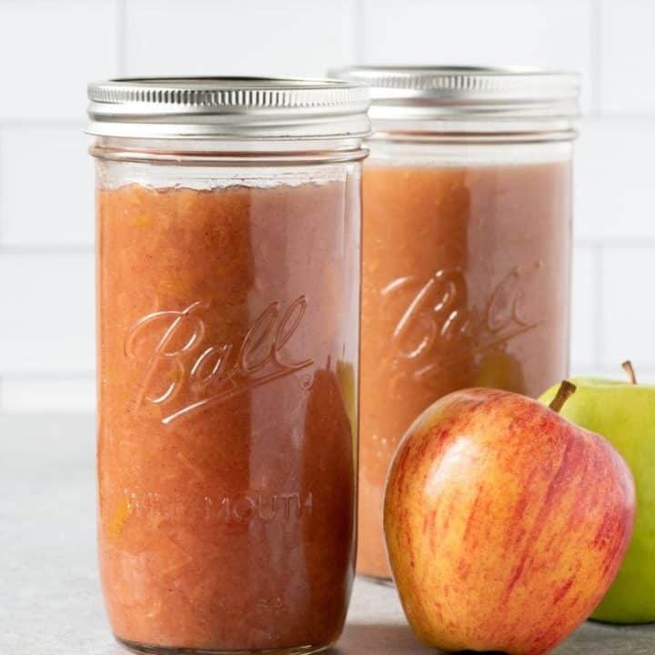 2 tall glass jars of Instant Pot Applesauce with some apples