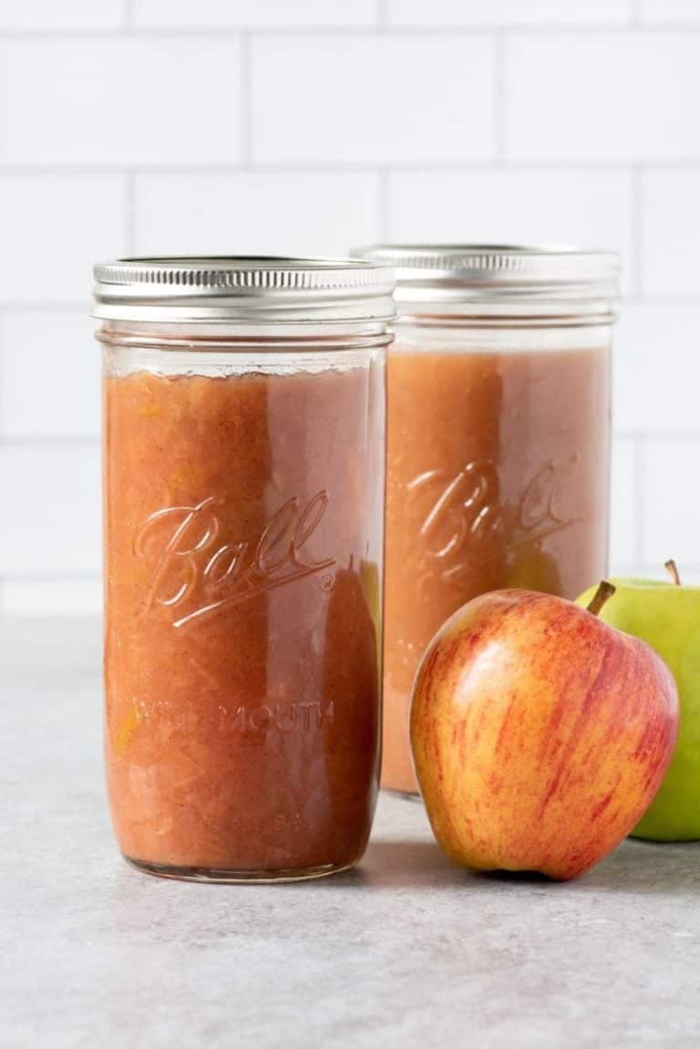2 tall glass jars of Instant Pot Applesauce with some apples