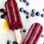 Blueberry Lemonade Frozen Fruit Pops on a bed of crushed ice, surrounded by blueberries and a cut lemon