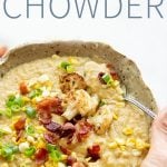 Hands holding a bowl full of Roasted Corn and Cauliflower Chowder, topped with corn, green onions, and bacon, with a text overlay