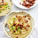 Two bowls full of Roasted Corn and Cauliflower Chowder, topped with corn, green onions, and bacon