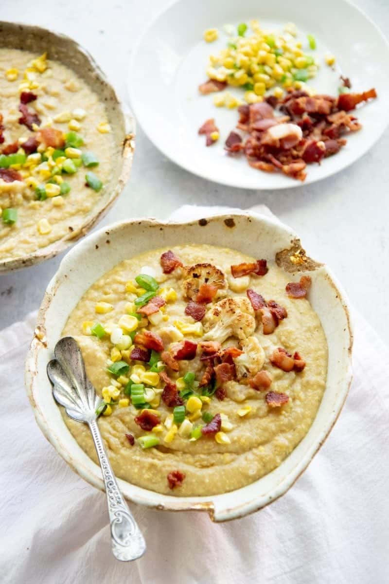 Two bowls full of Roasted Corn and Cauliflower Chowder, topped with corn, green onions, and bacon