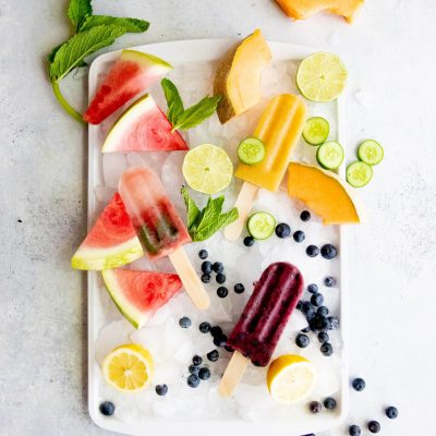 Overhead shot of three flavors of frozen fruit pops arranged on a tray of crushed ice, surrounded by fruit