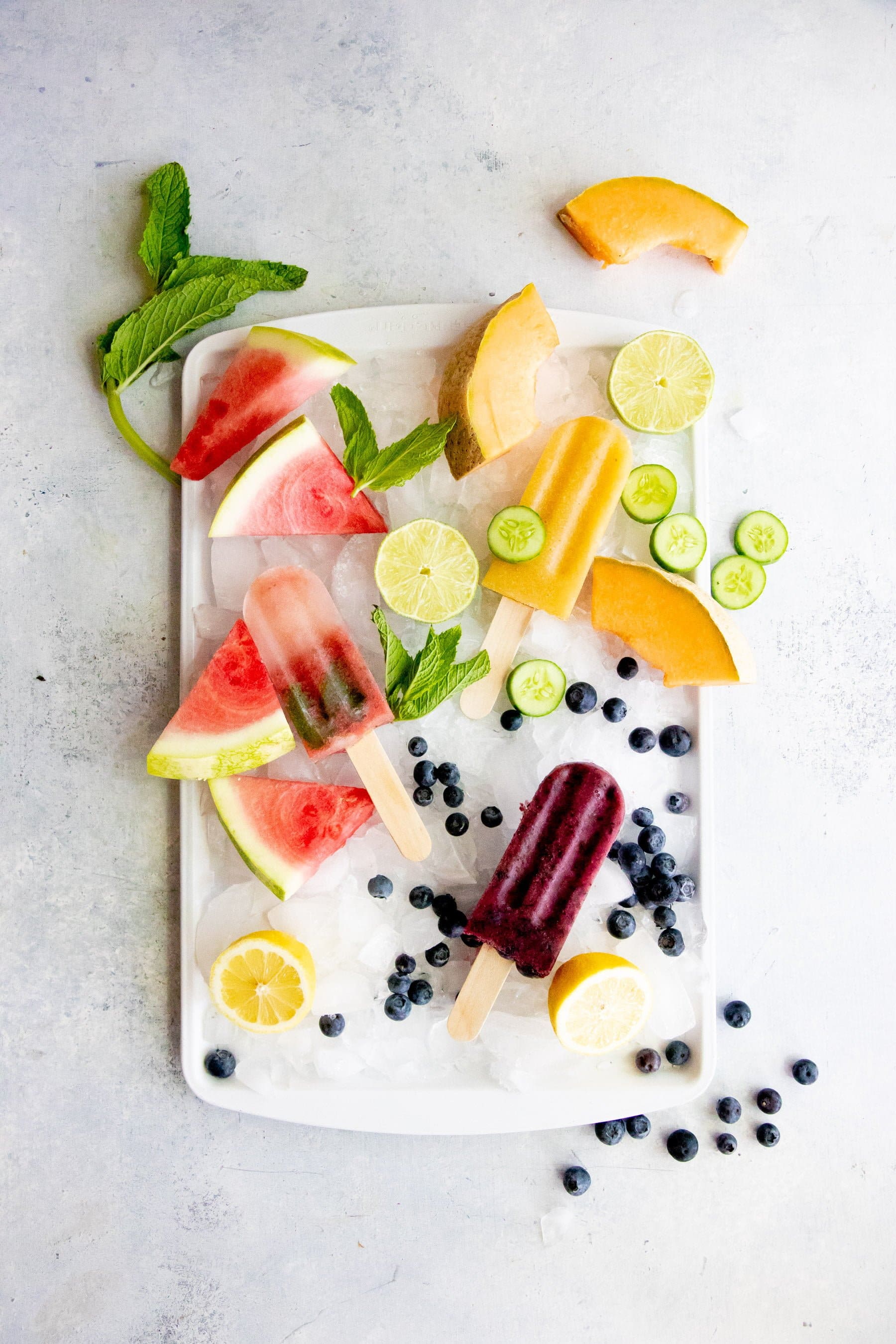 Overhead shot of three flavors of frozen fruit pops arranged on a tray of crushed ice, surrounded by fruit