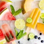Overhead shot of three flavors of frozen fruit pops arranged on a tray of crushed ice, surrounded by fresh fruit