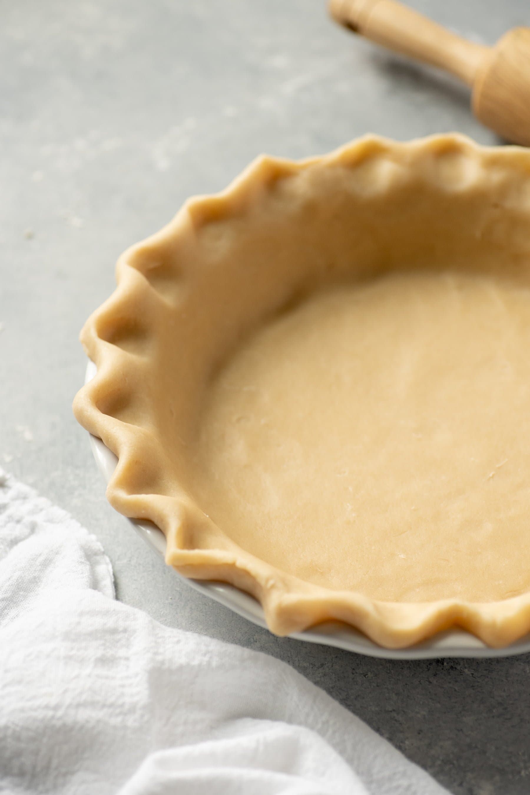Close-up of unbaked pie crust with fluted edges pressed into a pie pan on a gray background