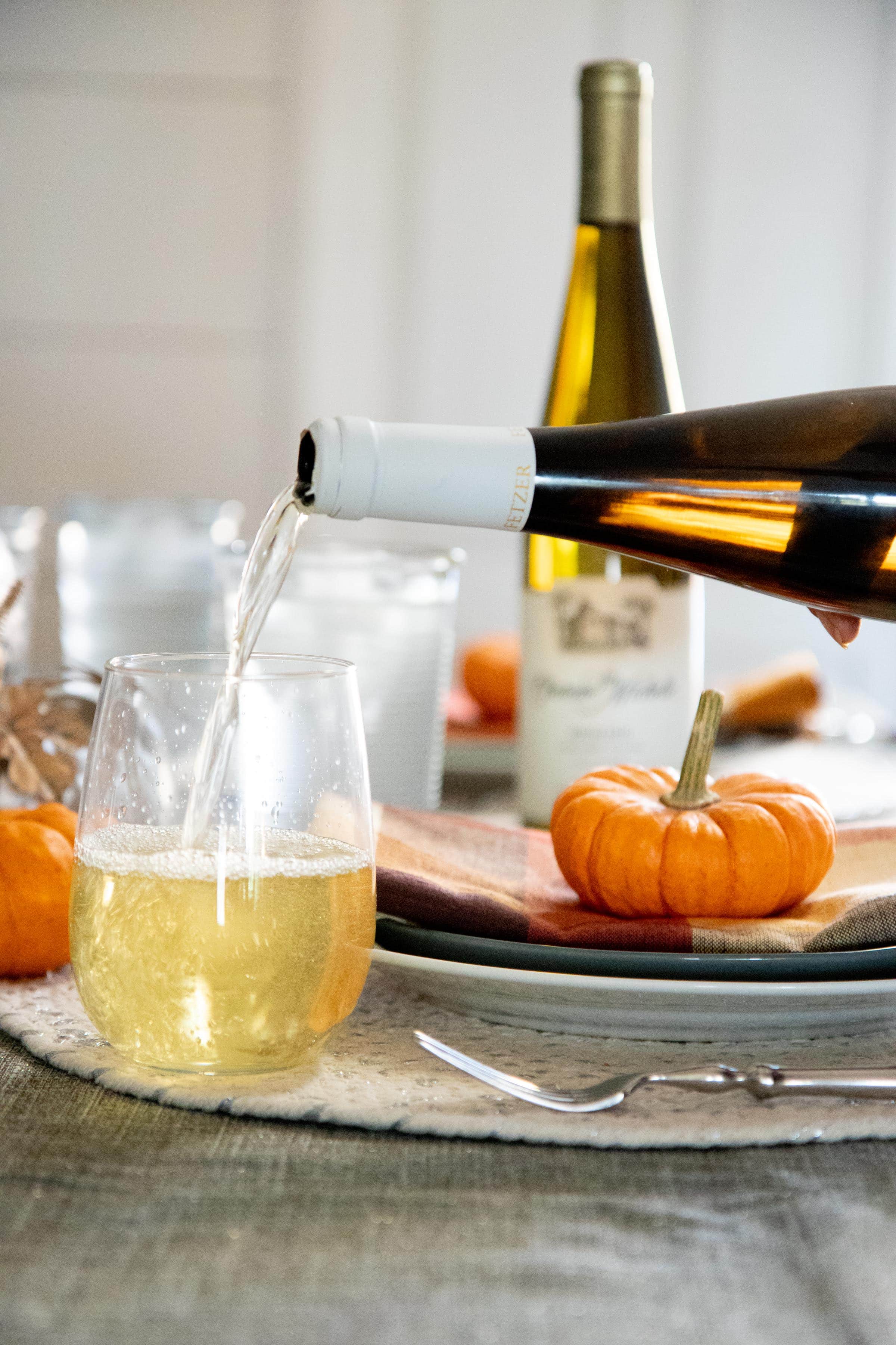 White wine being poured into a stemless glass on a table with fall decorations