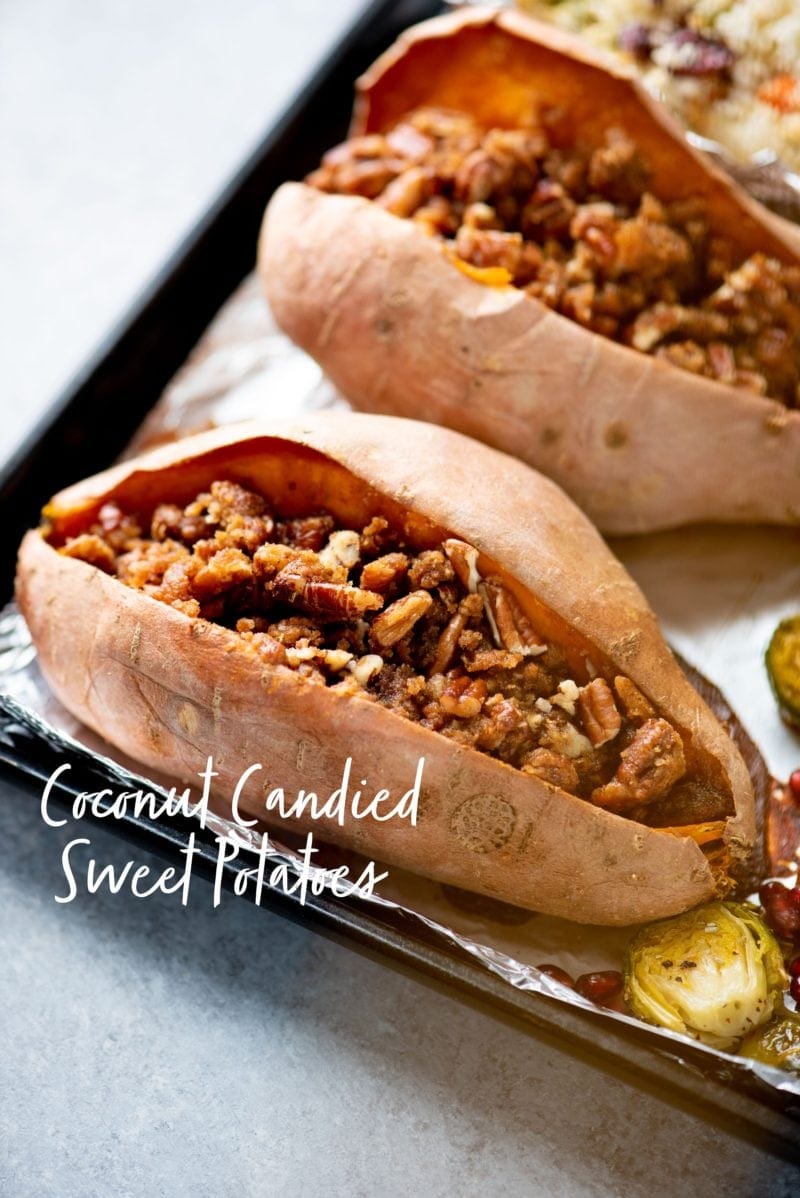 Two roasted sweet potatoes filled with nuts on a sheet pan. Text overlay reads "coconut candied sweet potatoes."
