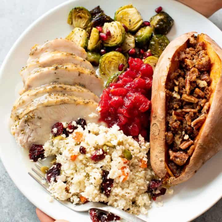 Hands holding a plate of Thanksgiving food - turkey, Brussels sprouts, cranberry sauce, sweet potatoes, and cauliflower rice pilaf