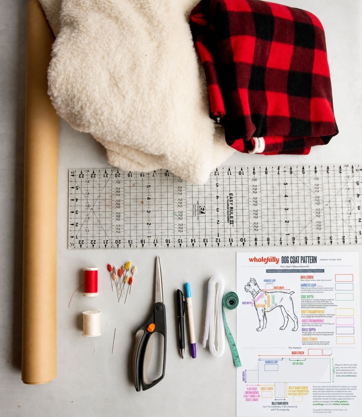 Materials laid out for a custom dog coat - fleece, faux fur, dog coat pattern paper, scissors, thread, pins, measuring tape, measurements sheet, and a ruler