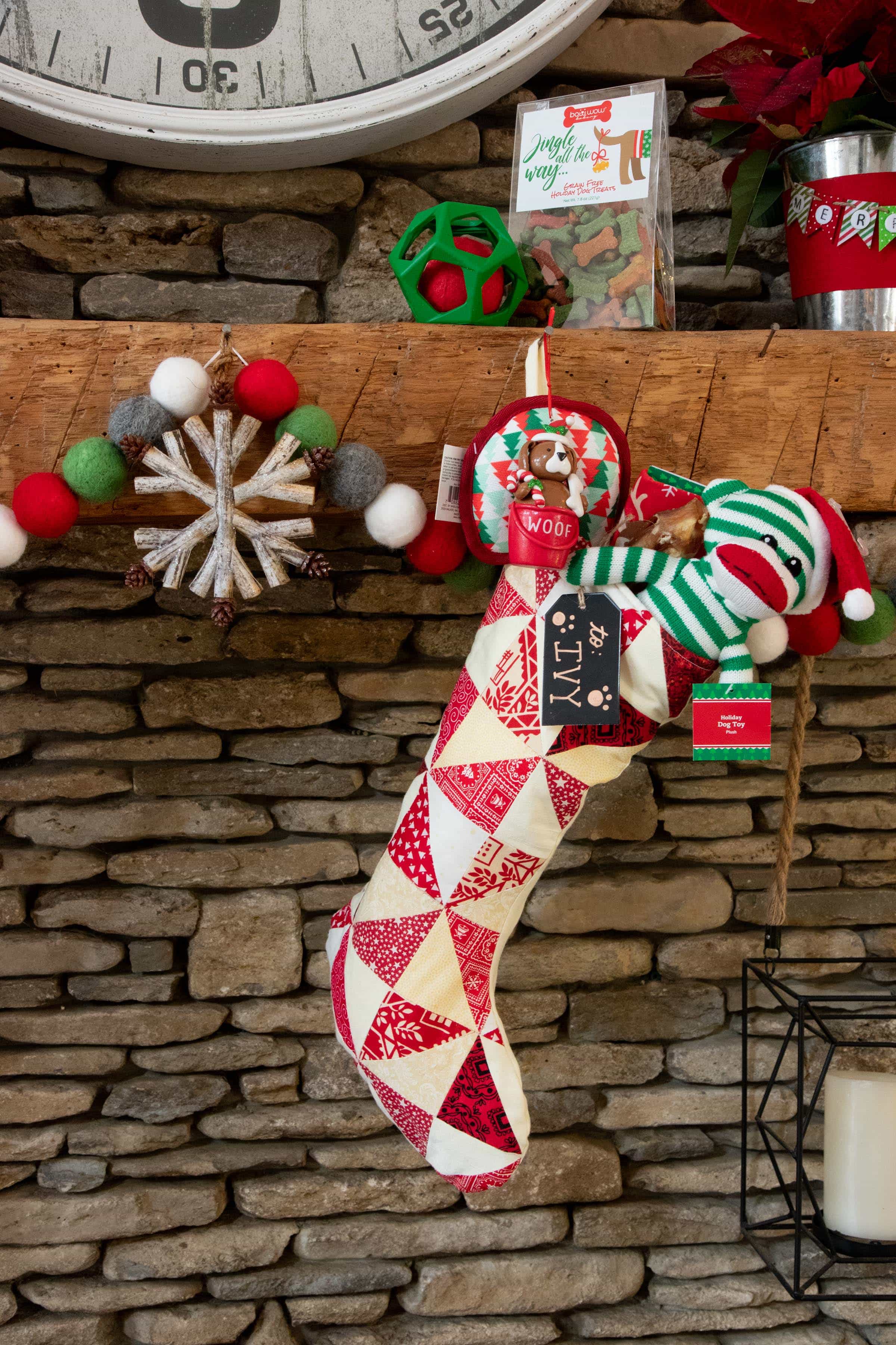 Red and white stocking filled with dog treats and toys hung on a mantle and tagged with "Ivy."