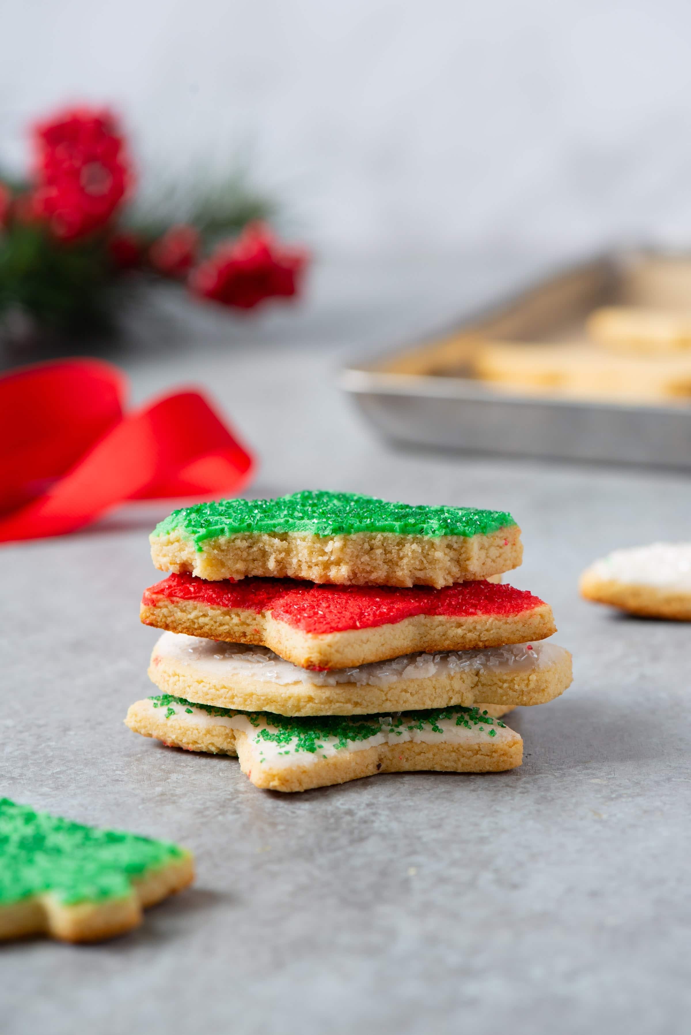 A stack of four grain-free paleo sugar cookies decorated with coconut butter frosting and Christmas sprinkles