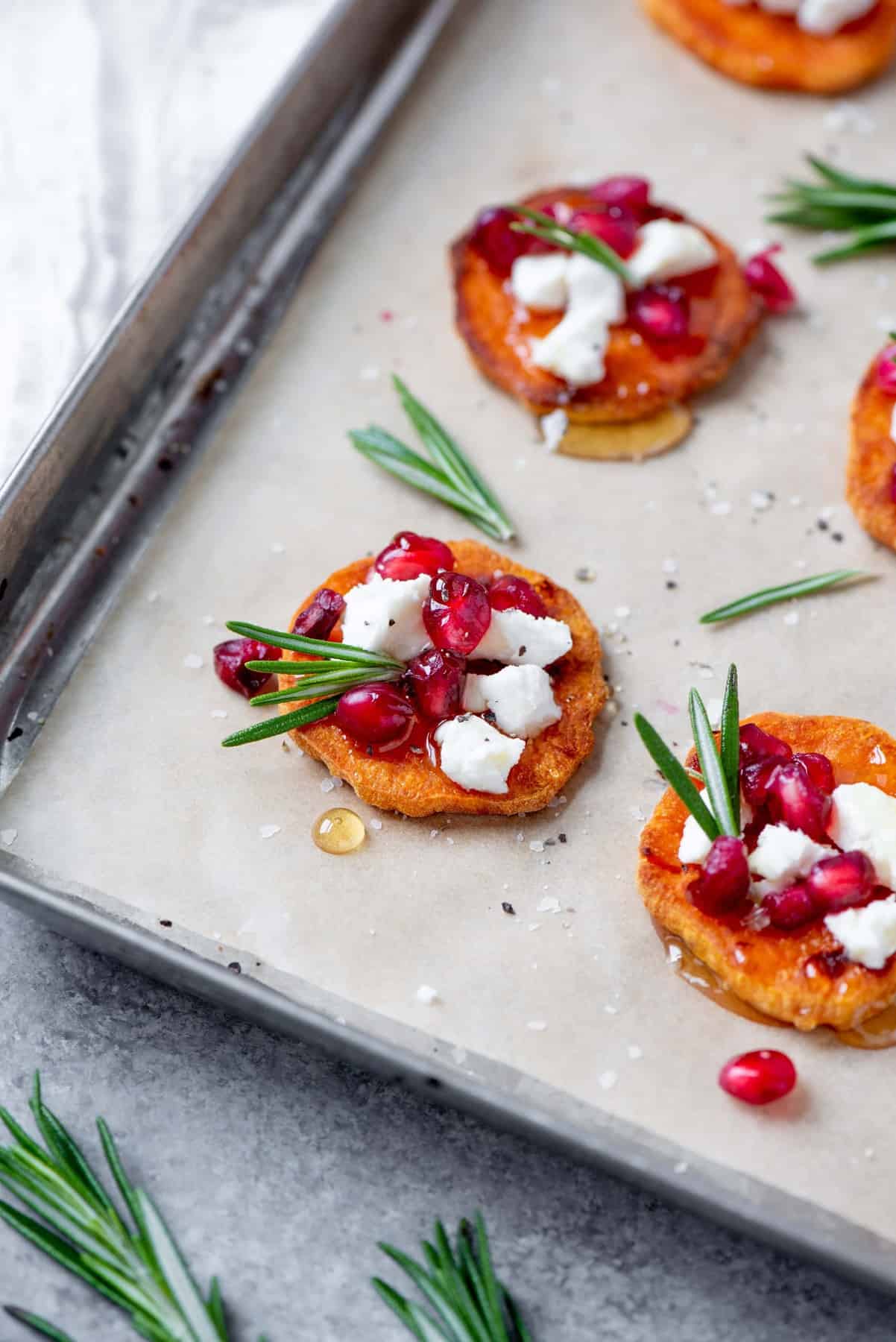 Assembled Sweet Potato Crostini with Goat Cheese and Pomegranate on a baking sheet lined with parchment paper