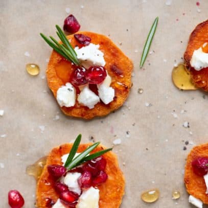 Close up of Sweet Potato Crostini with Goat Cheese and Pomegranate spread out on a baking sheet lined with parchment paper