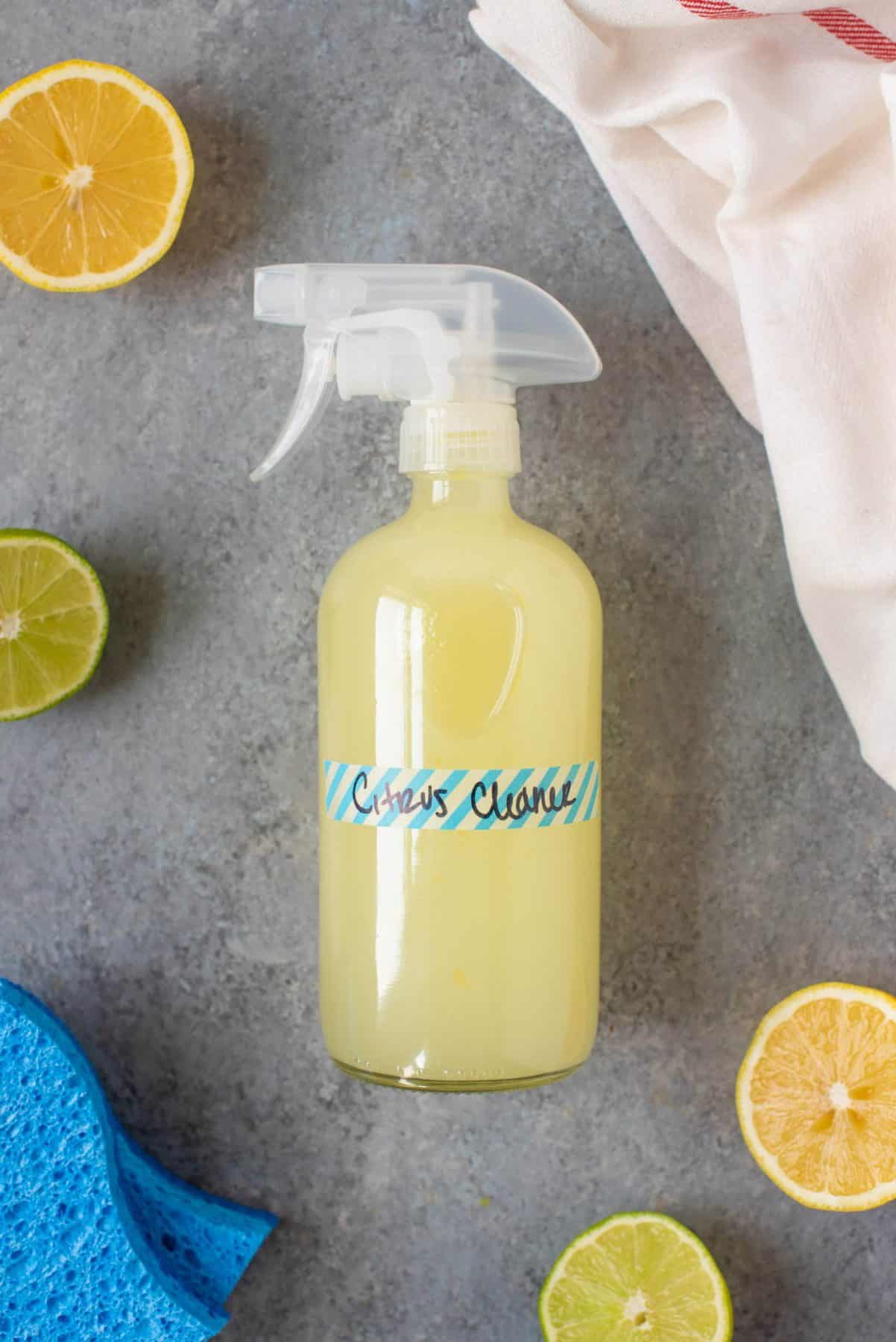 Spray bottle filled with Homemade Citrus All-Purpose Cleaner and labeled "Citrus Cleaner," surrounded by citrus and sponges