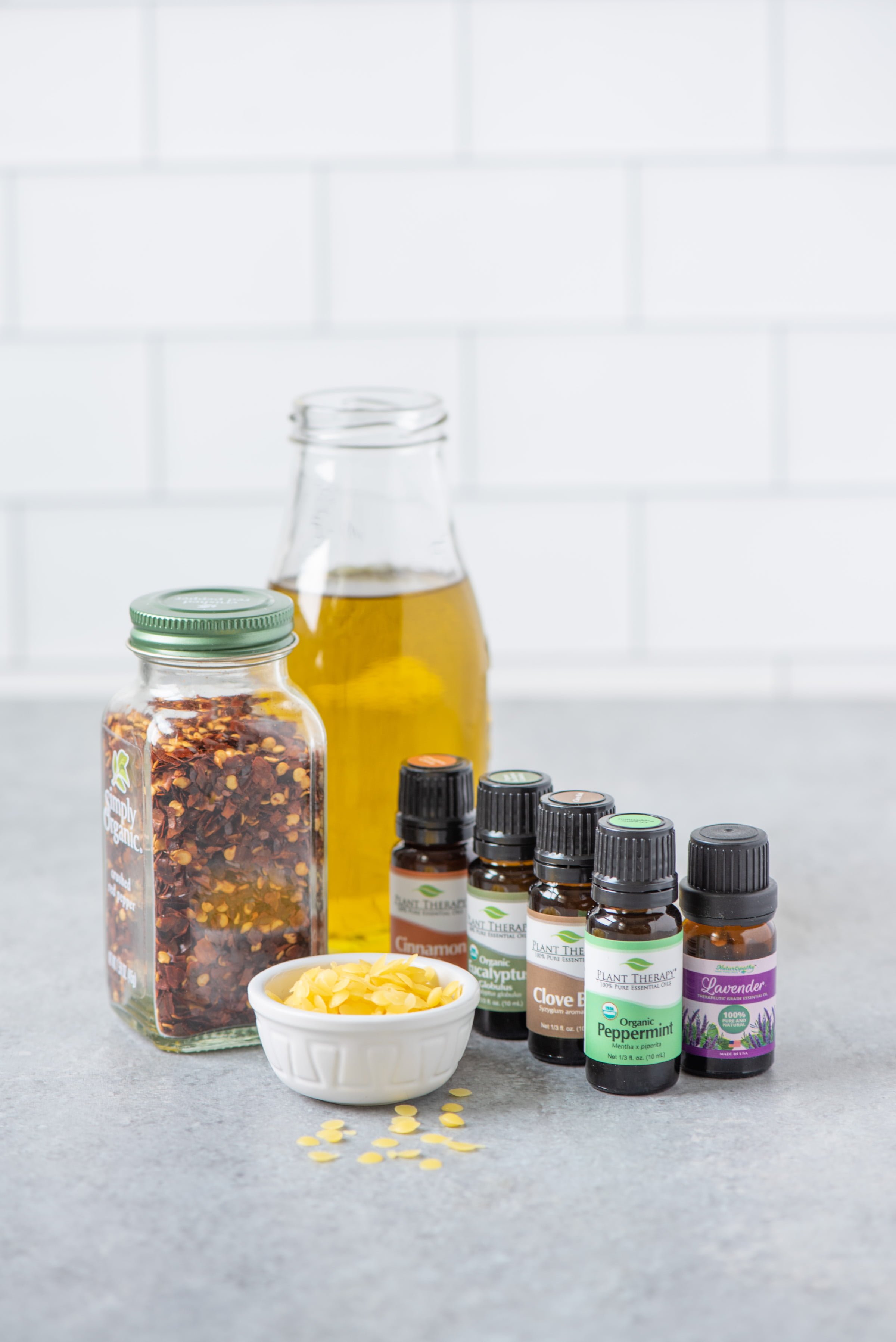Ingredients for DIY Hot and Cold Sore Muscle Rub arranged on a grey counter - oil, essential oils, red pepper flakes, and essential oils.