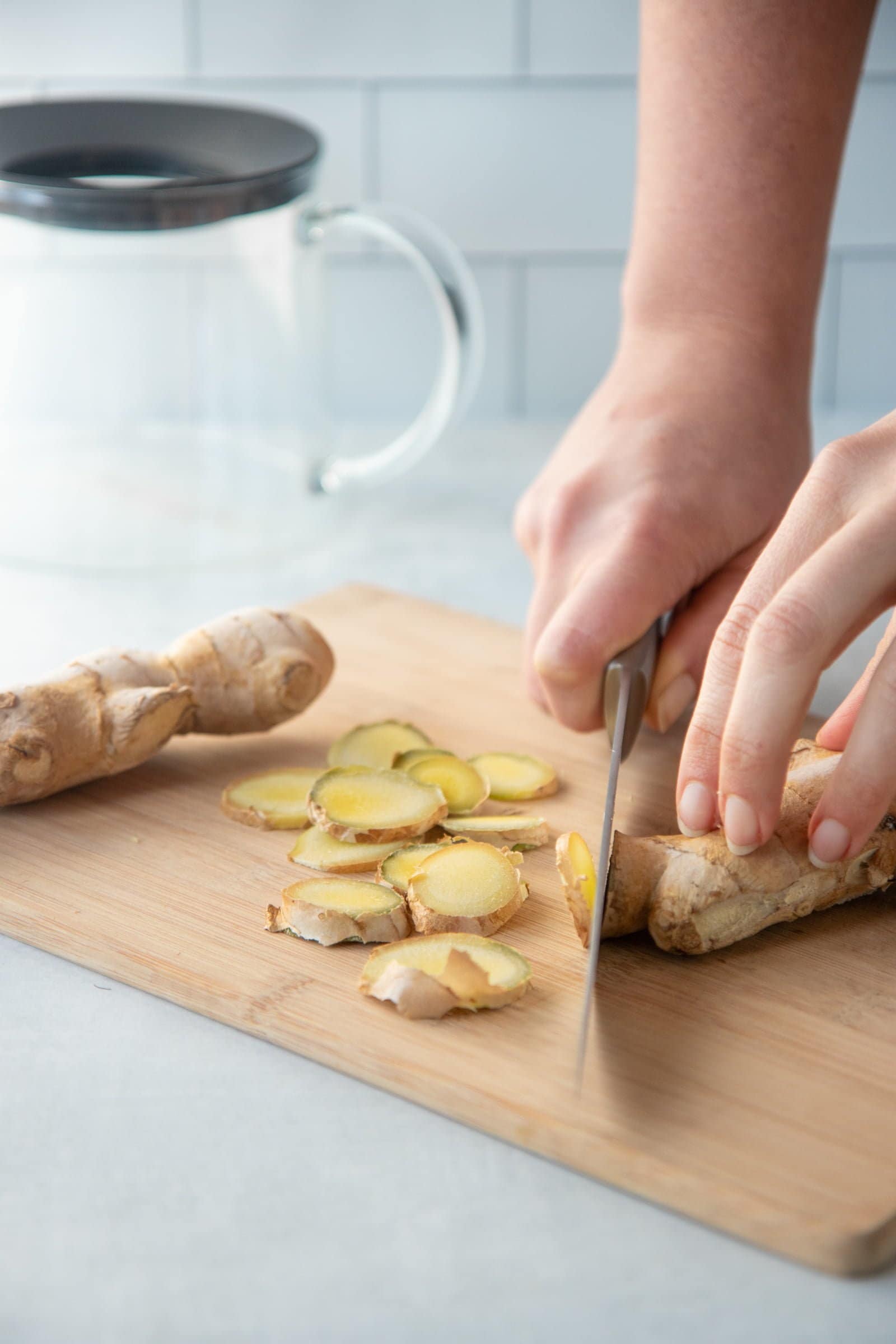 Hands slicing fresh ginger root on a wooden cutting board.