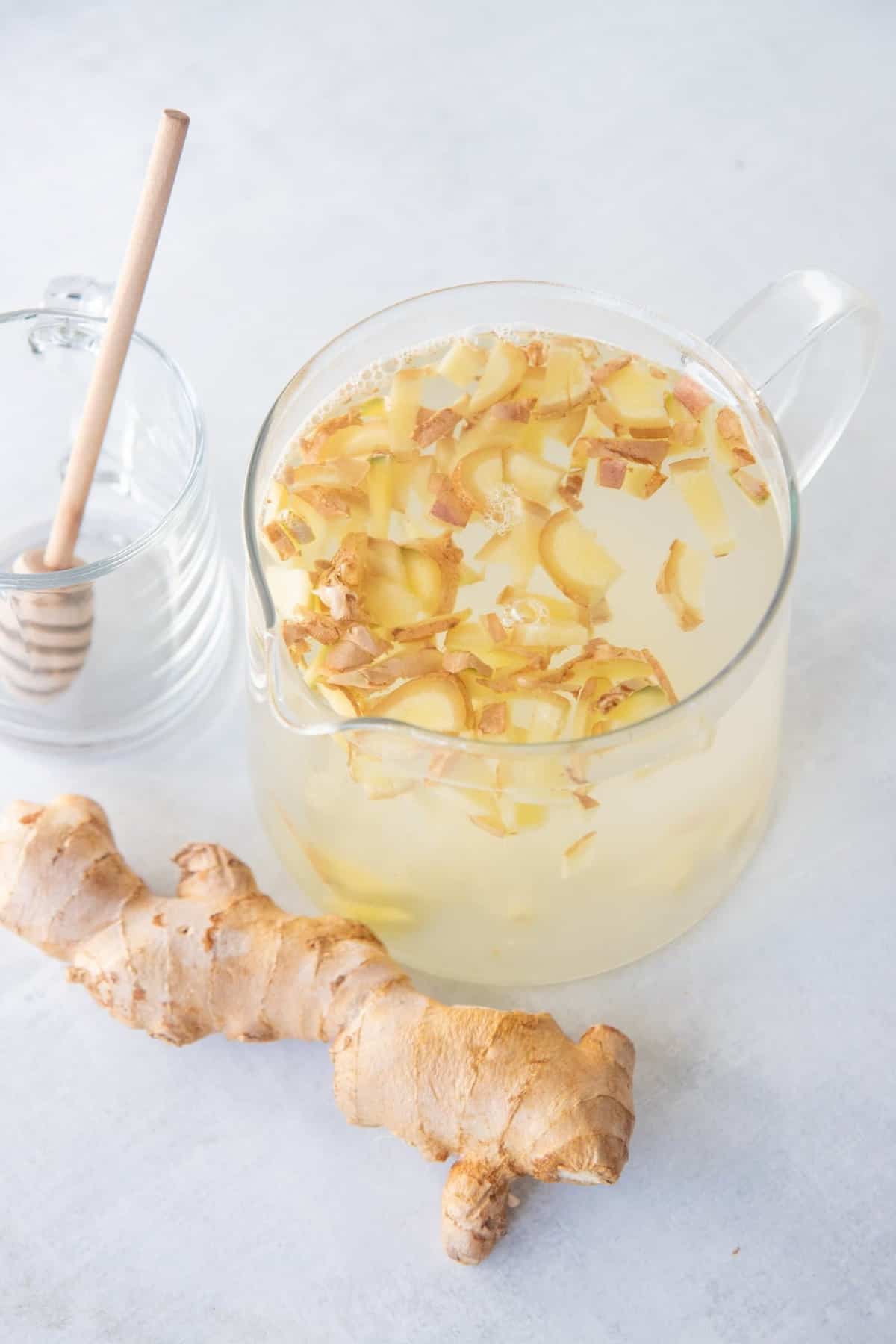 Top view of a large glass pitcher full of ginger tea with a fresh ginger root beside it.