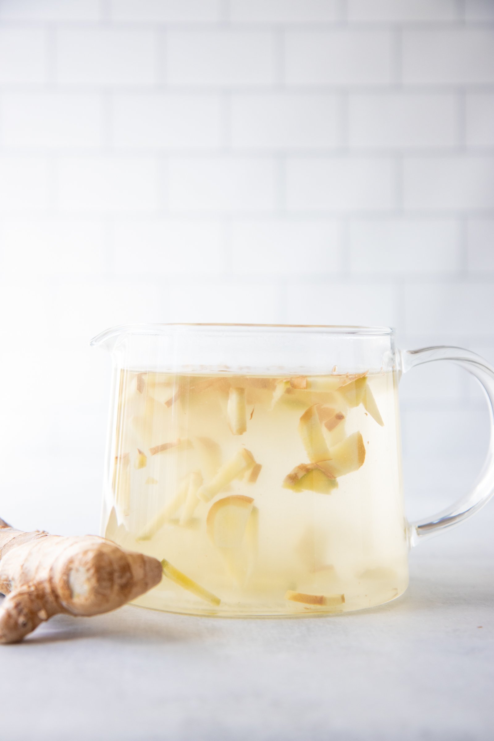 A large glass pitcher full of ginger tea made with fresh ginger root sits on a counter.